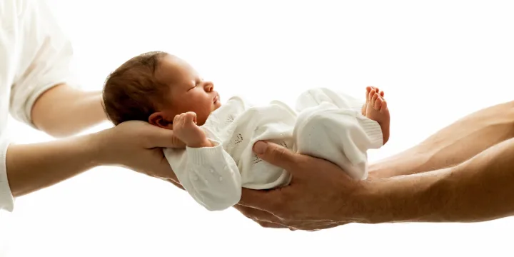 A newborn baby resting in a parent's cupped hands