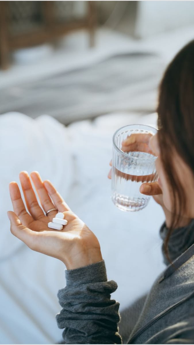 Woman taking folic acid supplement tablets with a glass of water